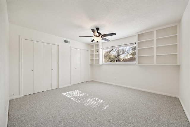 unfurnished bedroom featuring multiple closets, visible vents, a textured ceiling, and carpet floors