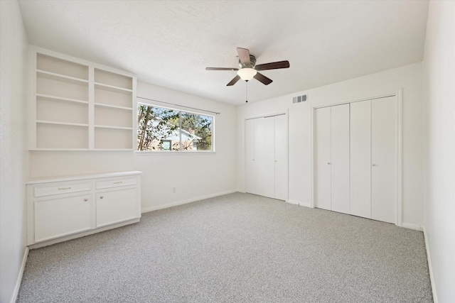 unfurnished bedroom featuring baseboards, two closets, visible vents, and light colored carpet