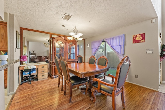 dining area featuring light hardwood / wood-style flooring, a textured ceiling, and a notable chandelier