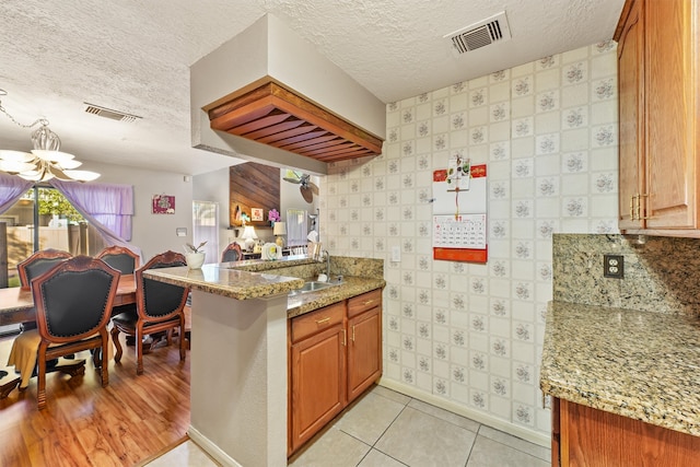 kitchen with light stone countertops, a notable chandelier, kitchen peninsula, a textured ceiling, and light wood-type flooring