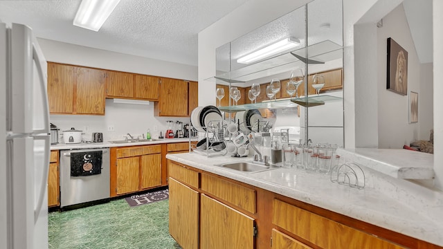 kitchen with a textured ceiling, white fridge, stainless steel dishwasher, and sink