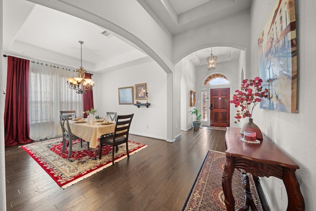 dining space with dark hardwood / wood-style floors, a tray ceiling, and a chandelier