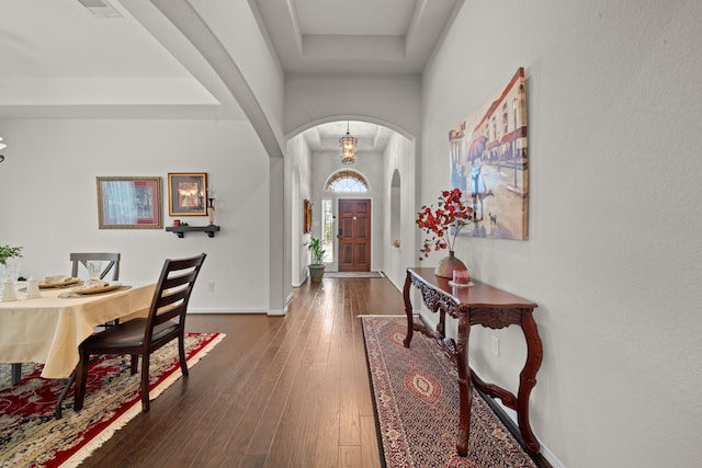 foyer entrance featuring an inviting chandelier, dark wood-type flooring, and a tray ceiling