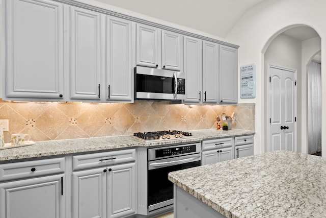 kitchen featuring light stone counters, lofted ceiling, stainless steel appliances, and tasteful backsplash