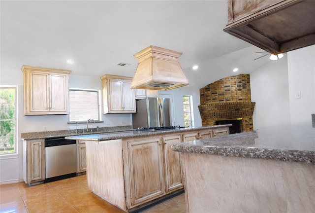 kitchen featuring light brown cabinets, lofted ceiling, light tile patterned floors, a fireplace, and stainless steel appliances