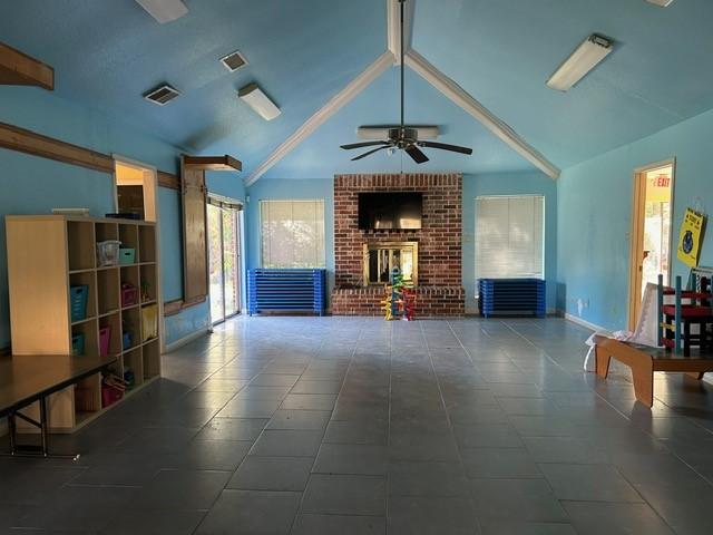 unfurnished living room featuring lofted ceiling with beams, ceiling fan, dark tile patterned floors, and a fireplace