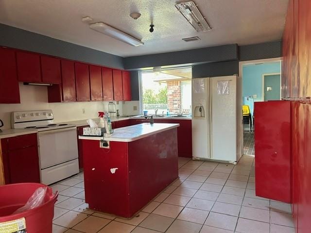 kitchen featuring a textured ceiling, light tile patterned floors, an island with sink, and white appliances