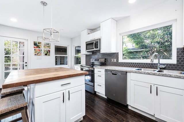 kitchen featuring appliances with stainless steel finishes, dark wood-type flooring, sink, white cabinetry, and hanging light fixtures