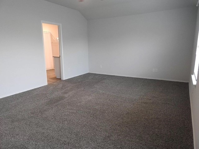 empty room with dark colored carpet and vaulted ceiling