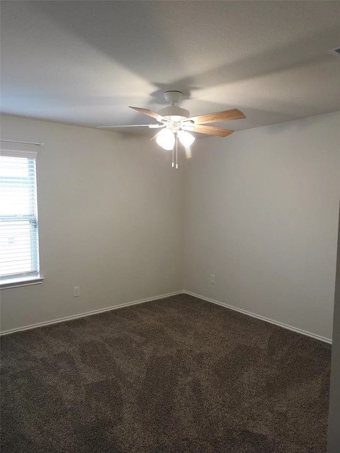 empty room with ceiling fan and dark colored carpet