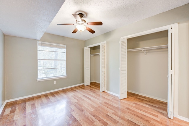 unfurnished bedroom with a textured ceiling, two closets, ceiling fan, and light hardwood / wood-style floors