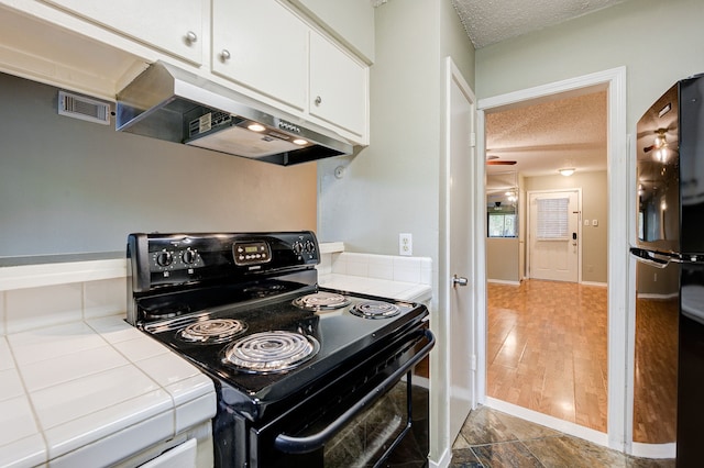 kitchen featuring stainless steel fridge, a textured ceiling, electric range, white cabinets, and tile counters