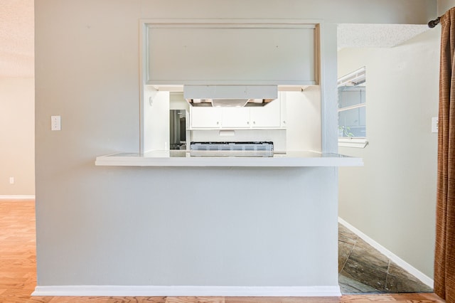 kitchen featuring kitchen peninsula, hardwood / wood-style floors, white cabinets, and ventilation hood