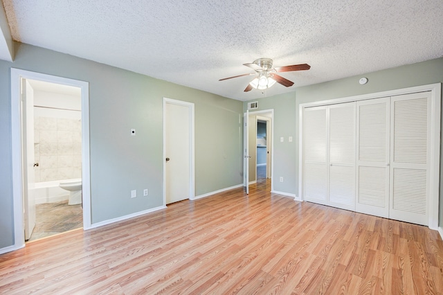 unfurnished bedroom with a textured ceiling, light wood-type flooring, ensuite bath, and ceiling fan