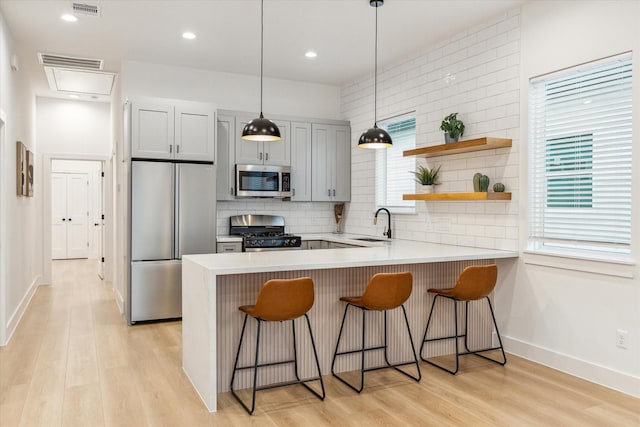 kitchen featuring decorative light fixtures, backsplash, kitchen peninsula, a breakfast bar area, and stainless steel appliances