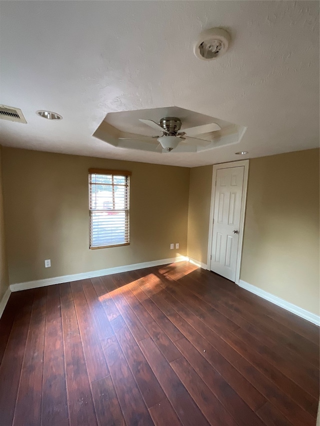 empty room with a raised ceiling, ceiling fan, and dark hardwood / wood-style flooring