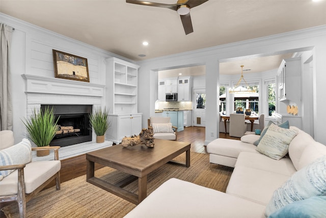 living room featuring hardwood / wood-style flooring, ceiling fan with notable chandelier, ornamental molding, and a fireplace