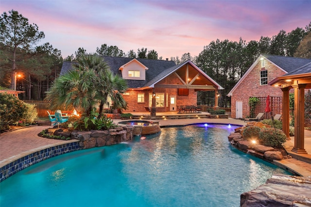 pool at dusk with an in ground hot tub, pool water feature, and a patio