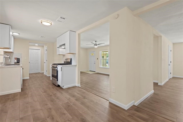 kitchen featuring light wood-type flooring, stainless steel gas stove, tasteful backsplash, and white cabinetry