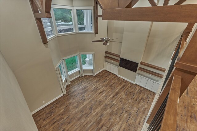 unfurnished living room with a wealth of natural light, baseboards, a towering ceiling, and wood finished floors