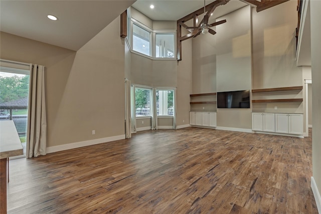 unfurnished living room featuring dark wood-type flooring, baseboards, ceiling fan, recessed lighting, and a high ceiling