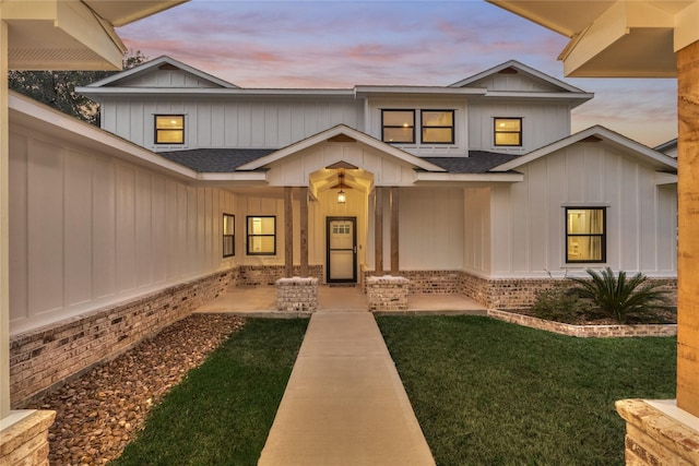 exterior entry at dusk featuring a yard, brick siding, and a shingled roof