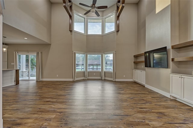 unfurnished living room featuring dark wood-type flooring, a ceiling fan, and baseboards