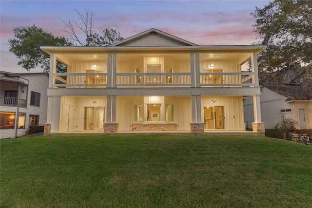 back of property at dusk featuring a lawn, board and batten siding, and a balcony