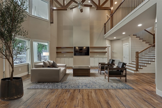 living room featuring wood finished floors, baseboards, a ceiling fan, a high ceiling, and stairs