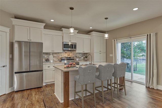 kitchen with a center island with sink, stainless steel appliances, decorative backsplash, light countertops, and white cabinets