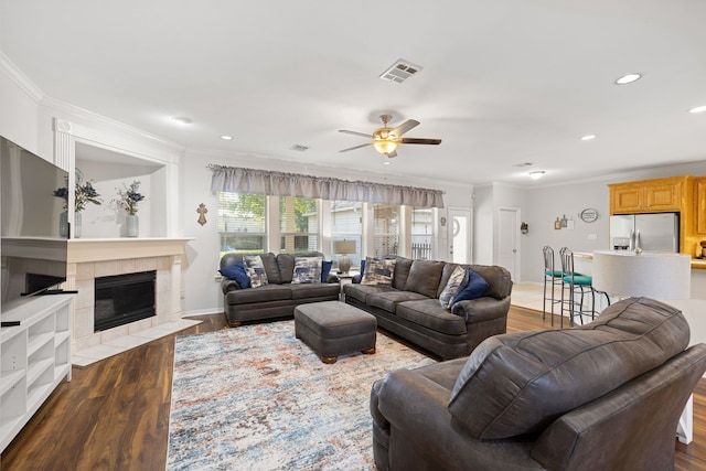 living room featuring a tile fireplace, crown molding, ceiling fan, and dark wood-type flooring