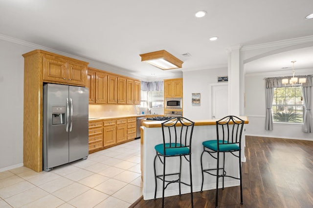 kitchen with ornamental molding, an inviting chandelier, stainless steel appliances, and light hardwood / wood-style floors