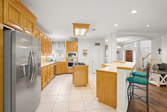 kitchen with a kitchen island, a kitchen bar, ornamental molding, and stainless steel appliances