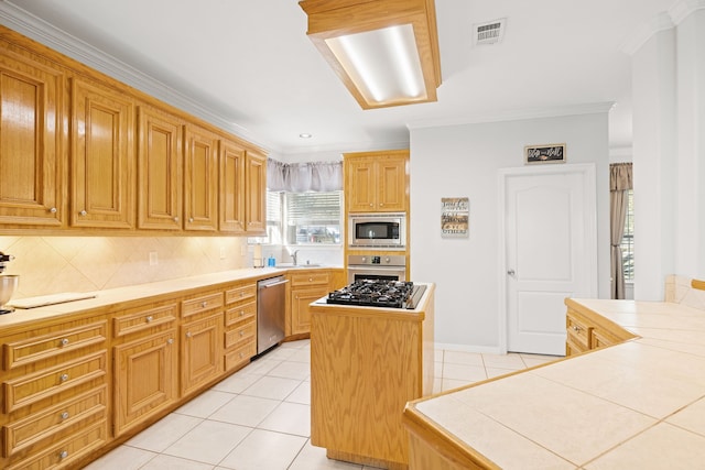 kitchen featuring decorative backsplash, appliances with stainless steel finishes, crown molding, a kitchen island, and tile counters