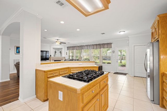 kitchen featuring a center island, black gas stovetop, crown molding, tile counters, and stainless steel refrigerator