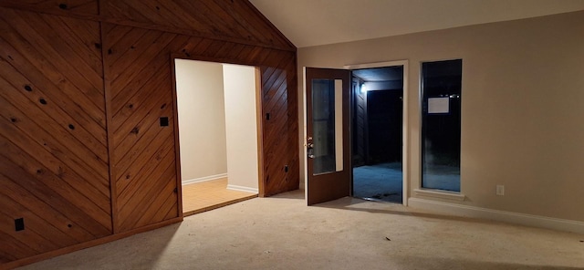 empty room with wood walls, light colored carpet, and vaulted ceiling