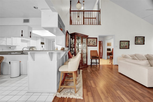 kitchen with high vaulted ceiling, kitchen peninsula, light hardwood / wood-style floors, a breakfast bar area, and white cabinets