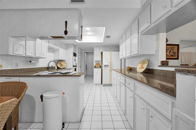 kitchen with white cabinetry, kitchen peninsula, white appliances, decorative backsplash, and light tile patterned floors