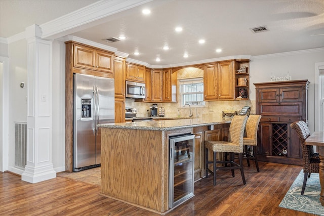 kitchen featuring beverage cooler, crown molding, wood-type flooring, a breakfast bar area, and appliances with stainless steel finishes