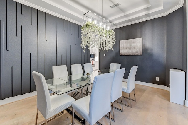 dining room with a raised ceiling, ornamental molding, and light wood-type flooring