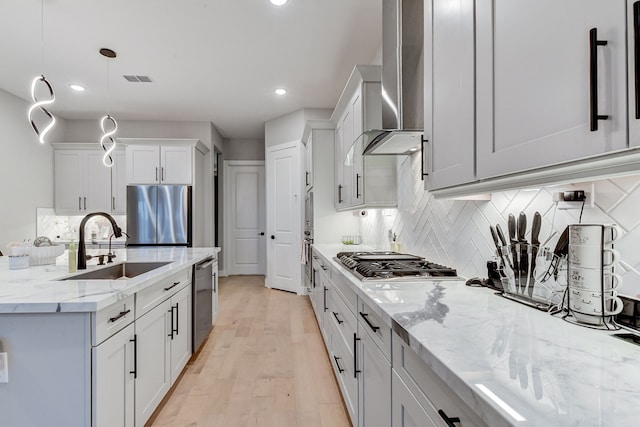 kitchen featuring pendant lighting, sink, light hardwood / wood-style flooring, wall chimney exhaust hood, and stainless steel appliances