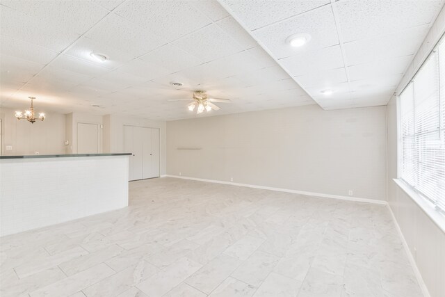 spare room featuring a drop ceiling and ceiling fan with notable chandelier