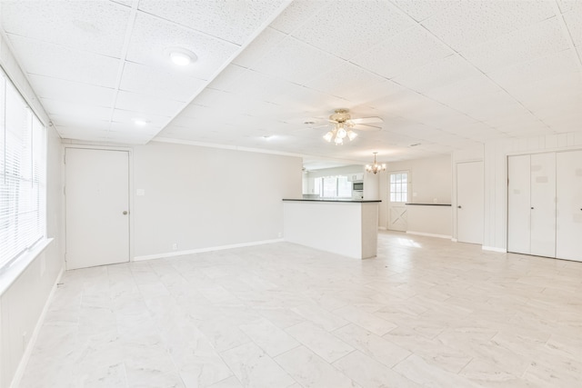 unfurnished living room with a drop ceiling and ceiling fan with notable chandelier