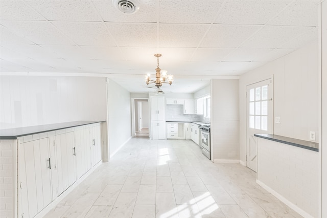 interior space with white cabinetry, a chandelier, pendant lighting, a paneled ceiling, and stainless steel range with gas stovetop