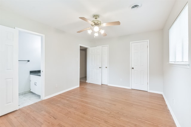 unfurnished bedroom with connected bathroom, ceiling fan, light hardwood / wood-style floors, and two closets