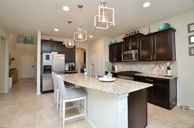 kitchen featuring a center island with sink, sink, appliances with stainless steel finishes, tasteful backsplash, and decorative light fixtures