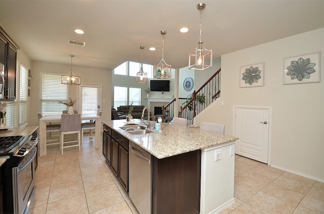 kitchen with sink, an island with sink, light stone counters, dark brown cabinetry, and stainless steel appliances