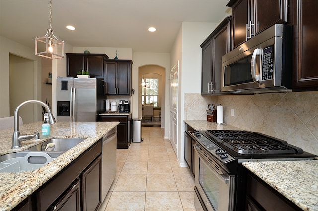 kitchen with pendant lighting, sink, decorative backsplash, light stone countertops, and stainless steel appliances