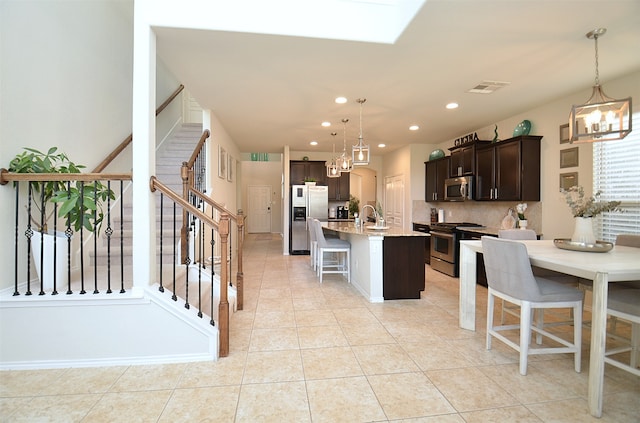 kitchen featuring a kitchen bar, dark brown cabinets, stainless steel appliances, hanging light fixtures, and an island with sink