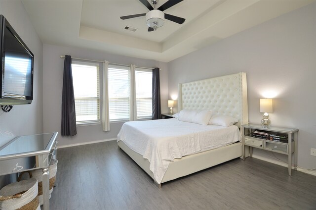 bedroom with dark hardwood / wood-style flooring, a tray ceiling, and ceiling fan